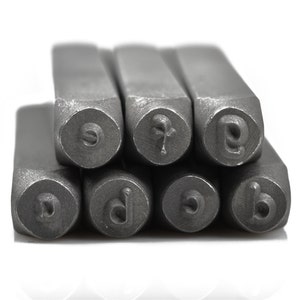 May include: Close-up of a set of metal letter stamps. The stamps are arranged in a stack, with the lettered ends facing the viewer. The letters visible are 'o', 'f', 'e', 'd', 'c', and 'b'. The stamps are made of a gray metal.