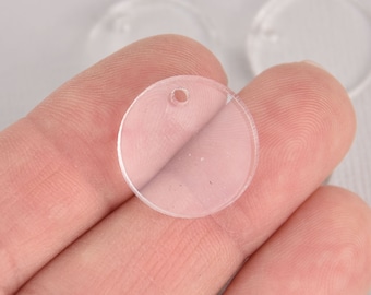 May include: Clear, round acrylic charms with a small hole for jewelry making or crafting. The charms are transparent and appear to be about 1 inch in diameter. Several charms are visible, with one held in a hand.