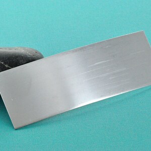 Op de afbeelding: Een geborsteld zilveren metalen plaat op een turquoise achtergrond.