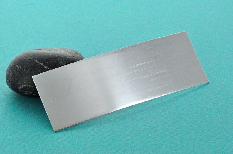 Op de afbeelding: Een geborsteld zilveren metalen plaat op een turquoise achtergrond.
