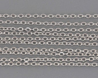 May include: Close-up of several strands of silver-colored oval link chain. The chains are arranged parallel to each other against a gray background. The links are uniform in size and shape, creating a repeating pattern.