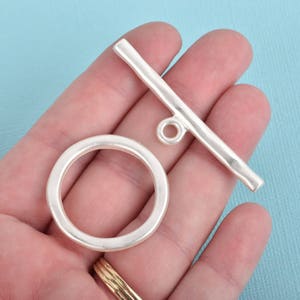 May include: Silver toggle clasp with a round ring. The clasp is a bar with a loop at one end and a round ring at the other end.