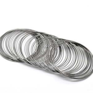 May include: A collection of silver-colored metal bangles, stacked and slightly fanned out against a white background. The bangles are thin and circular, creating a layered effect. The image is well-lit, highlighting the metallic sheen.