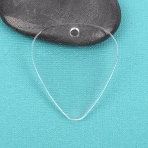May include: A clear plastic guitar pick with a hole at the top for a string or chain. The pick is shaped like a traditional guitar pick and is on a blue background.