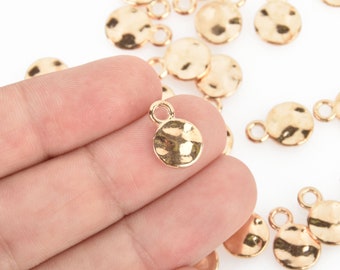 May include: Gold-toned metal circle charms with a hammered texture and a small loop at the top. The charms are scattered on a white surface.