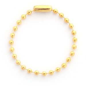 May include: A gold-colored ball chain with a cylindrical clasp. The chain is composed of small, round beads connected by thin wires. The clasp is a slightly darker gold color and has a rectangular shape.