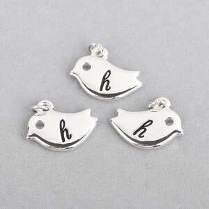 May include: Three silver bird charms, each with a small loop for hanging. The charms have a smooth, reflective surface and feature the lowercase letter "h" in black. The birds are stylized with a simple, rounded shape.