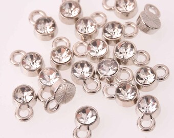 May include: A collection of clear crystal rhinestone charms with silver-toned metal loops. The charms are scattered on a white surface.
