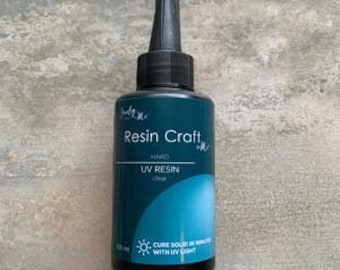 May include: A teal bottle of Resin Craft UV Resin, with a black nozzle and cap. The label includes the text "Resin Craft", "HARD UV RESIN", and "CURE SOLID IN MINUTES WITH UV LIGHT". The bottle contains 100 ml of clear resin.