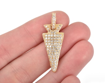 May include: A gold-colored pendant in the shape of an arrowhead, encrusted with small, clear gemstones. The pendant has a loop at the top for a chain. The arrowhead design is a popular jewelry motif.