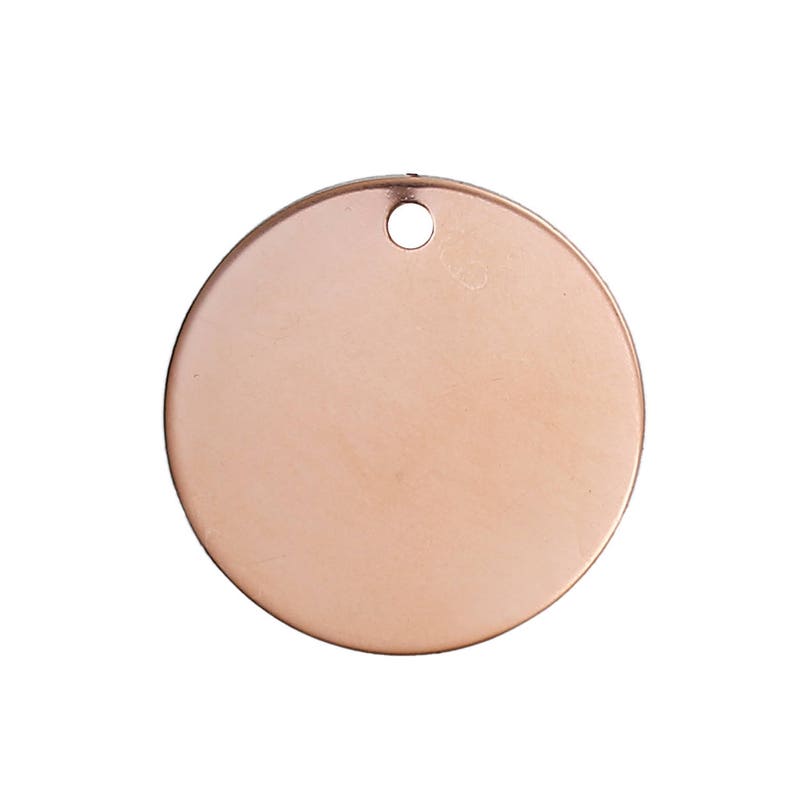May include: A blank, round, copper-colored metal tag with a small hole at the top for attaching to a chain or other item. The tag has a smooth, polished surface and is ready for engraving or stamping.