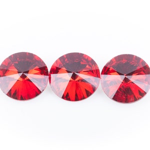 May include: Three round, faceted, red crystal rhinestones are arranged horizontally against a white background. The crystals have a brilliant, reflective quality, with multiple facets catching the light. These decorative crystals are suitable for crafts.