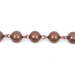 May include: A close-up of a copper chain with round beads. The chain is made of metal and has a shiny finish.