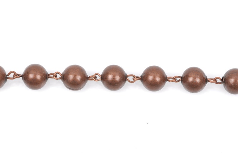 May include: A close-up of a copper chain with round beads. The chain is made of metal and has a shiny finish.