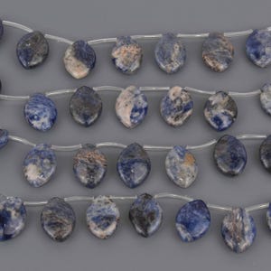 May include: Strands of teardrop-shaped sodalite beads in shades of blue, gray, and white. The beads are strung on clear cord, showcasing the natural patterns and variations in the stone. Ideal for jewelry making.