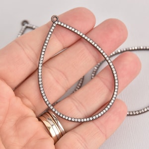 May include: A teardrop-shaped pendant with a silver-toned metal frame and a clear crystal border.