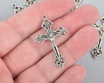 May include: Silver-toned metal crucifix pendant with intricate detailing. The cross features a figure of Jesus Christ and ornate floral and scrollwork designs. The pendant has a small loop at the top for attaching to a chain or cord.