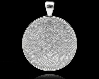 May include: A silver-colored pendant with a round, textured face and a small loop at the top. The pendant has a shiny, reflective surface and is set against a black background. The textured surface is made of many small, raised dots.