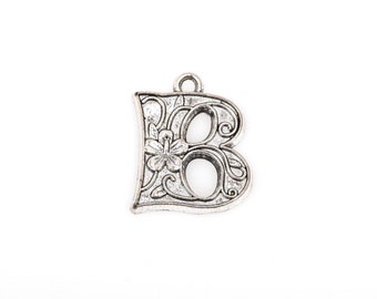 May include: A silver-colored metal charm in the shape of the letter "B". The charm features an ornate floral design with a small flower in the center. It has a loop at the top for attaching to a necklace or bracelet.