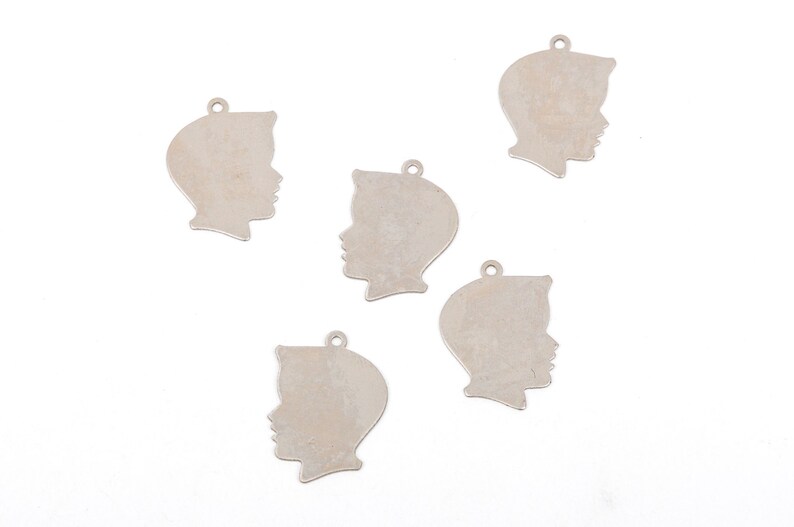 May include: Five silver metal charms shaped like a person's profile. The charms are blank and have a hole at the top for attaching to a necklace or bracelet.