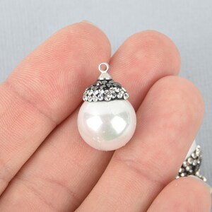 May include: A white pearl bead with a silver-colored cap adorned with black and clear crystals. The bead has a small loop at the top for stringing. The pearl has a slight iridescent sheen.