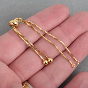 May include: Gold chain bracelet with a sliding clasp and two round beads. The bracelet is adjustable.