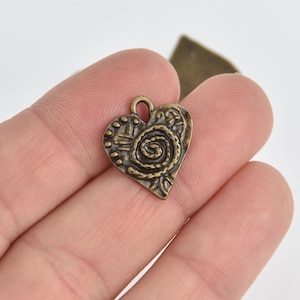 May include: A bronze heart-shaped charm with a detailed swirl design. The charm has a loop at the top for attaching to jewelry or other crafts.