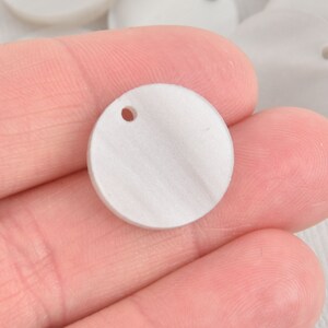 May include: White round ceramic pendant with a hole in the center. The pendant is smooth and has a slightly textured surface.