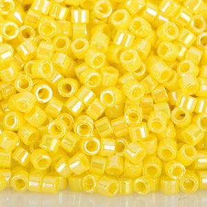 May include: A close-up shot of a pile of small, cylindrical yellow beads. The beads are uniform in shape and size, with a slightly translucent appearance. They are scattered across the surface, creating a textured, visually appealing display.