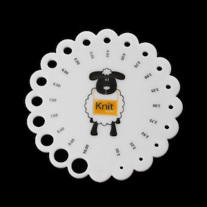 May include: A white, circular knitting needle gauge with a scalloped edge. It features a black and white sheep graphic with the text "Knit now" on a yellow tag. The gauge has numbered holes for measuring needle sizes.