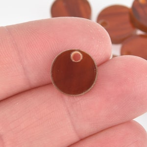 May include: A small, round, brown bead with a hole at the top. The bead has a smooth, glossy surface and a lighter brown edge. Other similar beads are visible in the background.