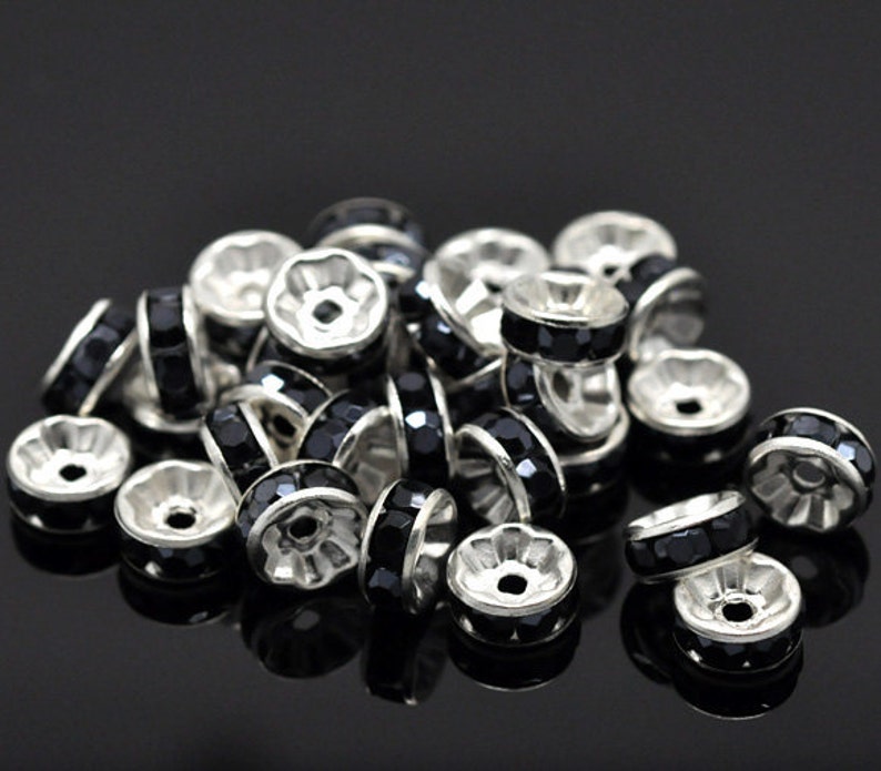 Puede incluir: Un mont&oacute;n de tapas de cuentas de metal plateadas con acentos de diamantes de imitaci&oacute;n negros. Las tapas de cuentas son redondas y tienen un peque&ntilde;o agujero en el centro.