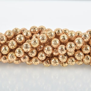 May include: Close-up of a strand of gold-colored, textured beads. The beads are spherical with a rough, pitted surface, giving them a unique, organic appearance. The beads are strung together, suggesting they are for jewelry making or crafting.