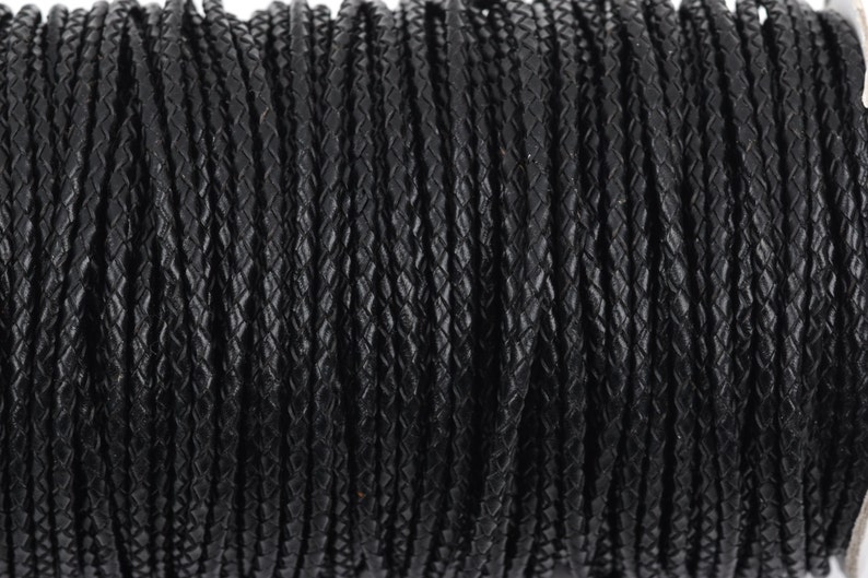 May include: Close-up of a spool of black braided leather cord. The cord is tightly wound and has a textured surface.