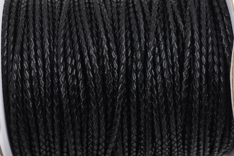 May include: A close-up of a spool of black braided leather cord. The cord has a textured, diamond-shaped pattern.