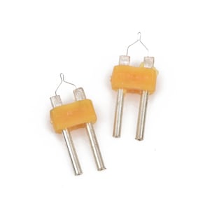 May include: Two small, yellow and silver-colored electrical components are displayed against a white background. Each component has two silver pins, a yellow rectangular body, and a small wire loop at the top.