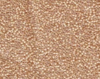 May include: Close-up of a pile of small, round, light-tan seed beads. The beads are densely packed together, creating a textured surface. The beads appear to be made of glass or a similar material, with a slightly translucent quality.