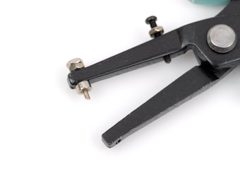 May include: Close-up of a black hole punch tool with a teal handle. The tool has a black metal frame with a silver screw and a small, pointed tip. The tool is designed for making holes in various materials.