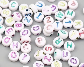 Può includere: Assortimento di perline di plastica bianche a forma di lettere dell'alfabeto con accenti di lettere arcobaleno. Le perline sono disposte in uno schema casuale.