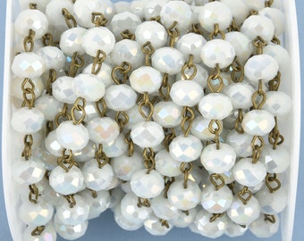 May include: A spool of white faceted beads strung on antique brass-colored chain. The beads have an iridescent quality, reflecting multiple colors. This jewelry-making supply is ideal for necklaces, bracelets, and other crafts.