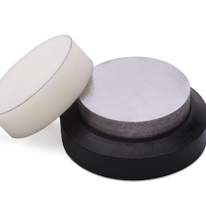 May include: A jewelry-making tool set featuring a black base, a silver metal disc, and a white, oval-shaped piece. The pieces are designed for shaping and forming metal. The set is used in jewelry making and metalworking.