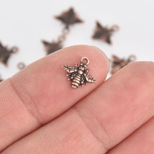 May include: A close-up of a copper-toned bee charm with a detailed design. The charm has a loop at the top for attaching to jewelry or other crafts.