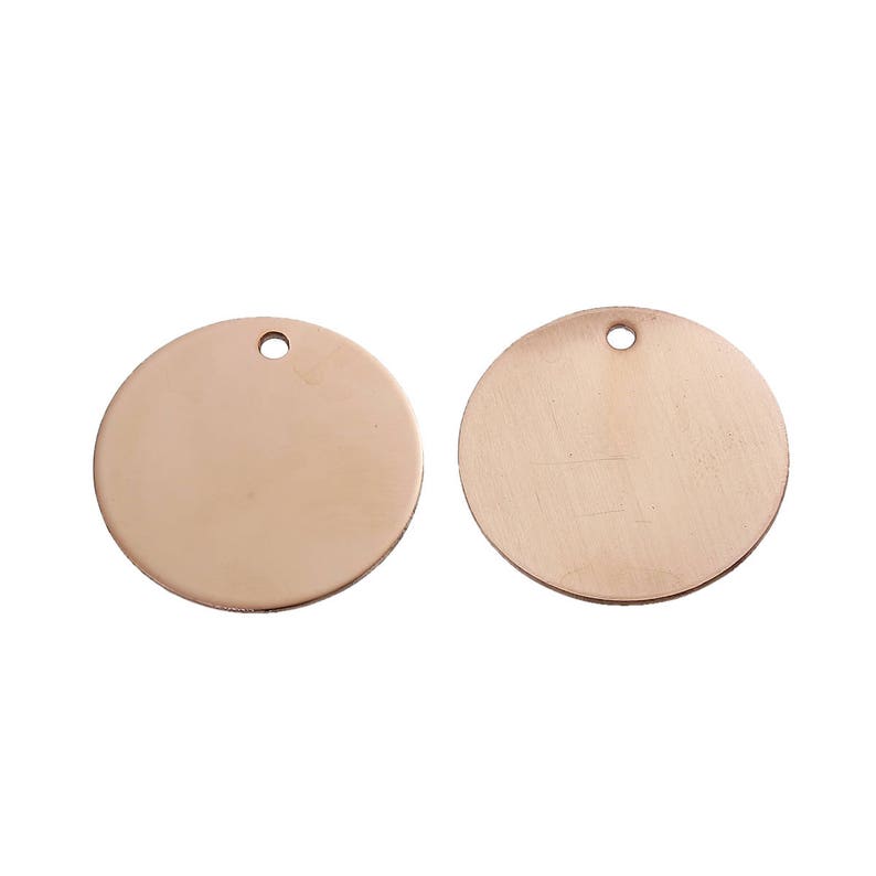 May include: Two blank, rose gold-colored metal circle pendants with a small hole at the top for stringing. The pendants are smooth and shiny, perfect for jewelry making or crafting projects.