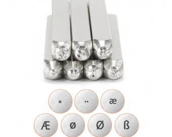 May include: A set of metal letter and symbol stamps for crafting. The stamps are silver-colored and include letters, numbers, and punctuation marks. The set also includes circular metal stamps with special characters.