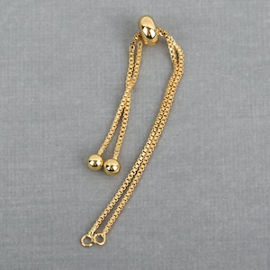 May include: Gold-toned chain with two round beads and a loop at the top. The chain is designed to be used as a necklace extender or bracelet extender.