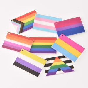 May include: A collection of rectangular pride flag designs in various colors. Flags include the rainbow, transgender, bisexual, lesbian, pansexual, non-binary, and progress pride flags. Each flag has a small hole at the top.