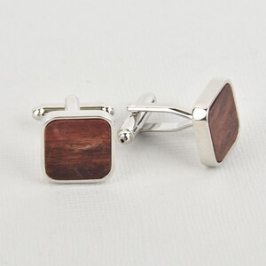 May include: A pair of square cufflinks with a silver-tone metal frame and a dark brown wood inlay. The cufflinks have a classic design, suitable for formal wear or adding a touch of sophistication to any outfit.