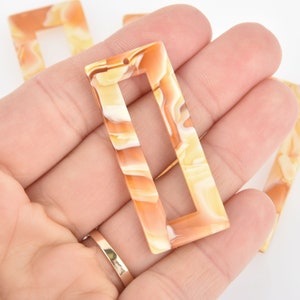 May include: A set of four rectangular, marbled, plastic, decorative pieces with a hole at the top. The pieces are a mix of light brown and white.