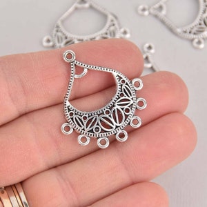 May include: Silver-toned metal earring findings with a teardrop shape and intricate filigree design. The findings have a loop at the top for attaching a hook or other jewelry component. There are six small loops around the bottom of the teardrop.