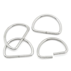 May include: Four silver-colored D-rings, each with a half-circle shape. One ring is interlocked with another, while the remaining three are separate. The rings are made of a shiny, metallic material.
